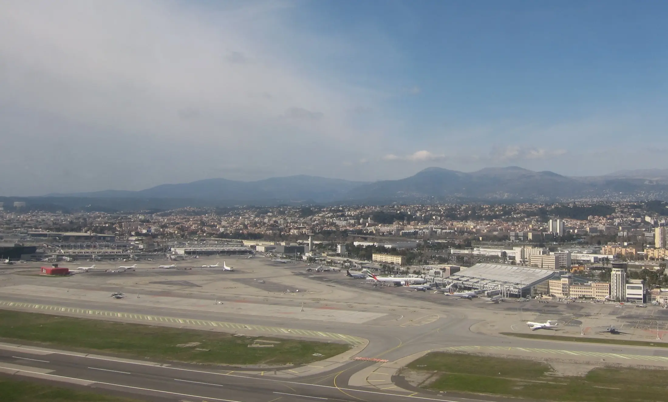 Les pistes et les terminaux de l'aéroport Nice Côte d'Azur, avec les collines de Nice derrière